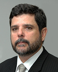 Imagem em plano americano mostra o ministro do TST Guilherme Augusto Caputo Bastos em pose clássica de estúdio, olhando para a câmera