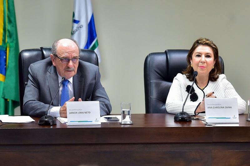 Imagem: Fotografia do ouvidor do TRT-PR, desembargador Arnor Lima Neto, vestino de terno cinza com gravata azul, homem calvo, fala ao microfone em frente a uma mesa; ao lado da diretora da Escola Judicial, desembargadora Ana Carolna Zaina, mulher branca de cabelos até altura do ombo, veste blusa branca. (arquivo JPG)