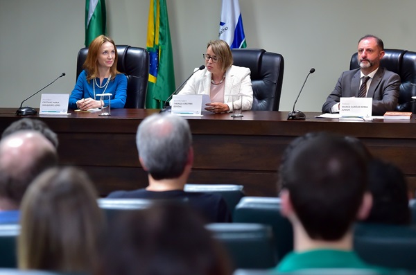 Imagem: Fotografia mostra três pessoas sentadas em frente à mesa do evento: duas mulheres e um homem: a partir da esquerda, procuradora do MPT, Cristiane Sbalqueiro Lopes; a desembargadora Thereza Gosdal, mediadora; e o professor de Direito da UFPR, Marcus Aurélio Serau Júnior. No primeiro plano, cabeças de pessoas na plateia. (arquivo JPG)