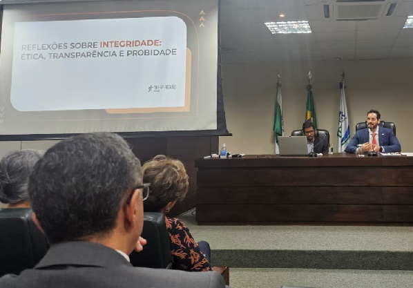 Imagem: fotografia mostra dois homens sentados em frente a bancada de madeira e, em frente, um grupo de pessoas de costas acompanha a fala. Ao lado, um projetor com uma imagem escrito: Reflexões sobre integridade: ética, transparência e probidade. (arquivo JPG) Imagem: fotografia mostra dois homens sentados em frente a bancada de madeira e, em frente, um grupo de pessoas de costas acompanha a fala. Ao lado, um projetor com uma imagem escrito: Reflexões sobre integridade: ética, transparência e probidade. (arquivo JPG)